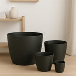 Set of black plant pots on a wooden floor with a light-colored wall in the background.