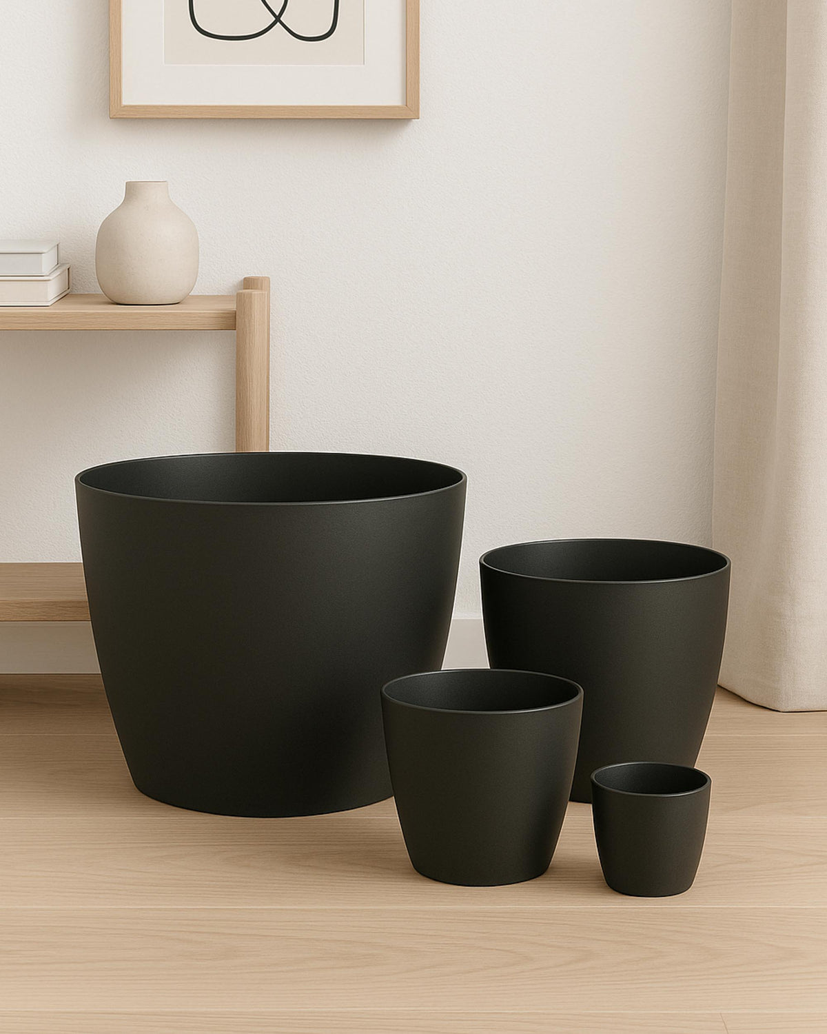 Set of black plant pots on a wooden floor with a light-colored wall in the background.