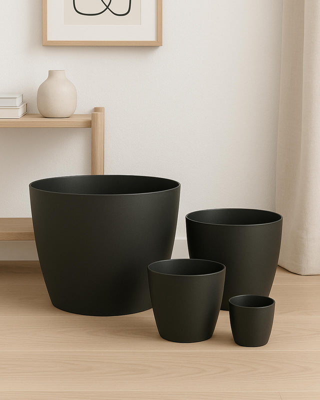Set of black plant pots on a wooden floor with a light-colored wall in the background.