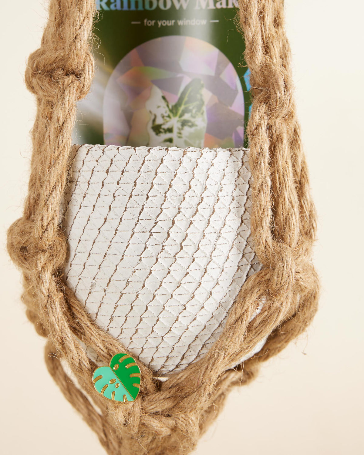Macrame plant hanger with a small green leaf charm on a beige background