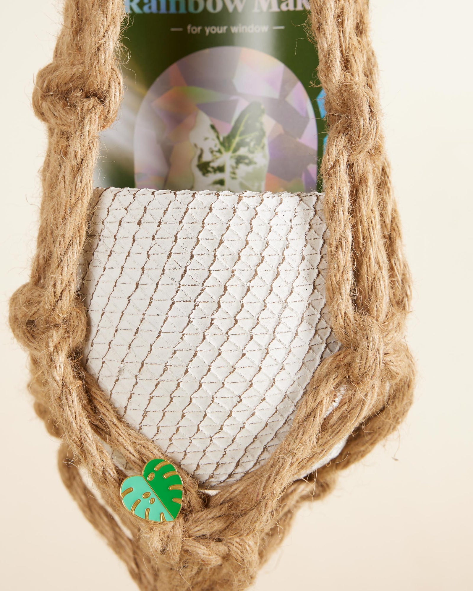Macrame plant hanger with a small green leaf charm on a beige background