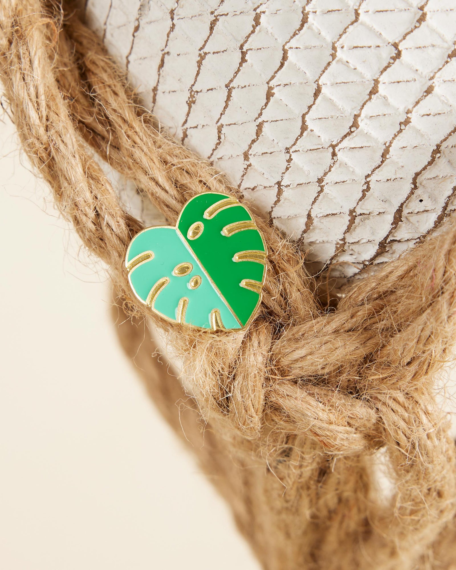 Green leaf-shaped pin on braided rope with a textured background