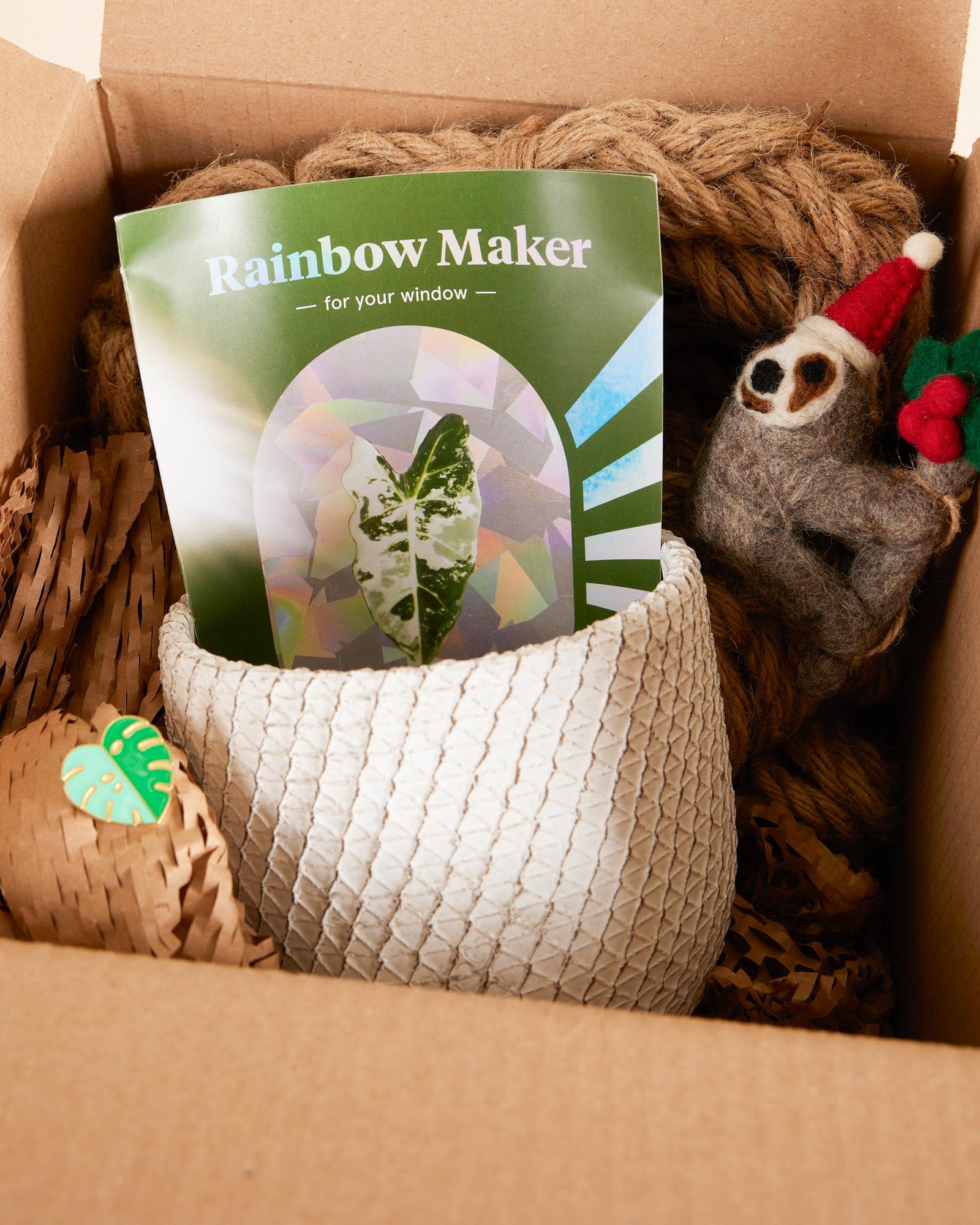 Box containing a 'Rainbow Maker' book, a woven basket, and a sloth toy.